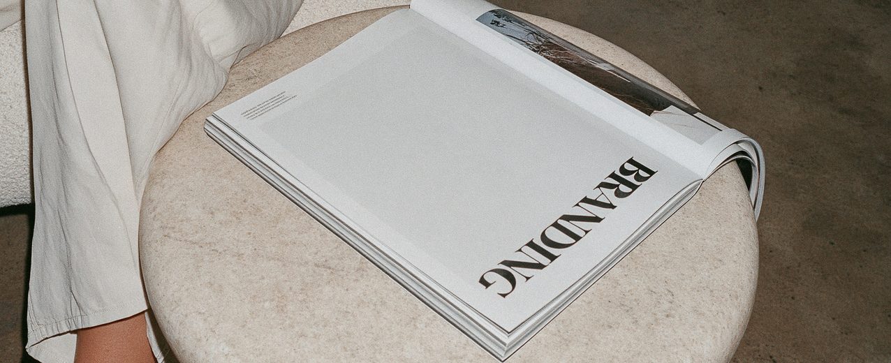 A magazine titled Branding resting on a stone stool beside a person in cream trousers.