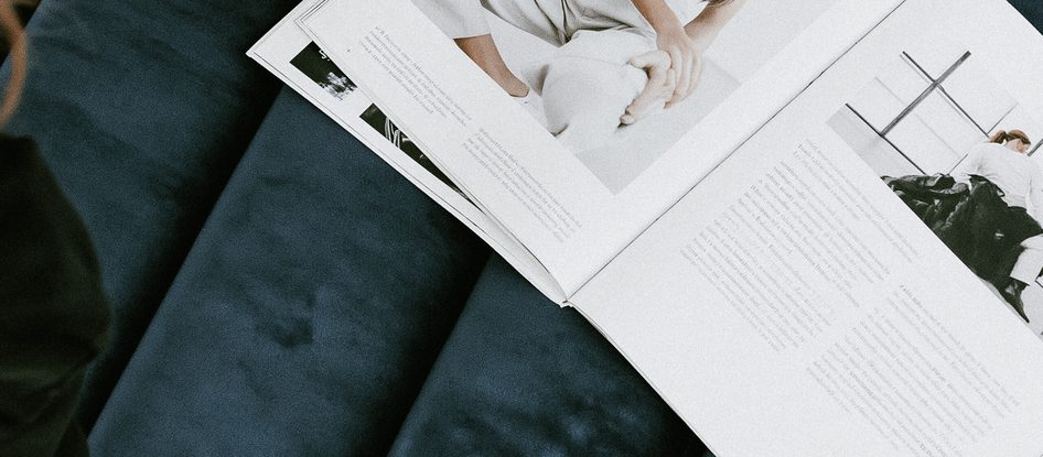 Hands opening a printed magazine spread on a navy velvet sofa.