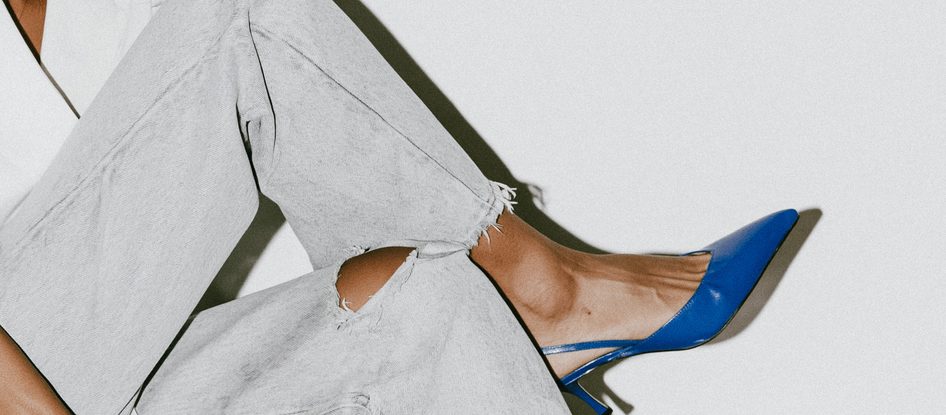 A close-up of a blue heeled shoe worn with pale jeans on a stone step.