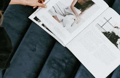 Hands opening a printed magazine spread on a navy velvet sofa.
