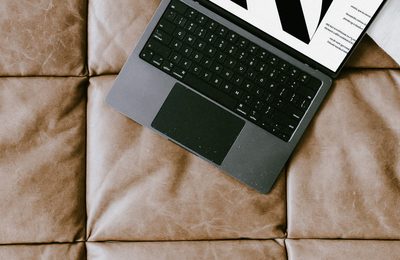 An open laptop on a tan leather sofa, with a printed page beside the keyboard.
