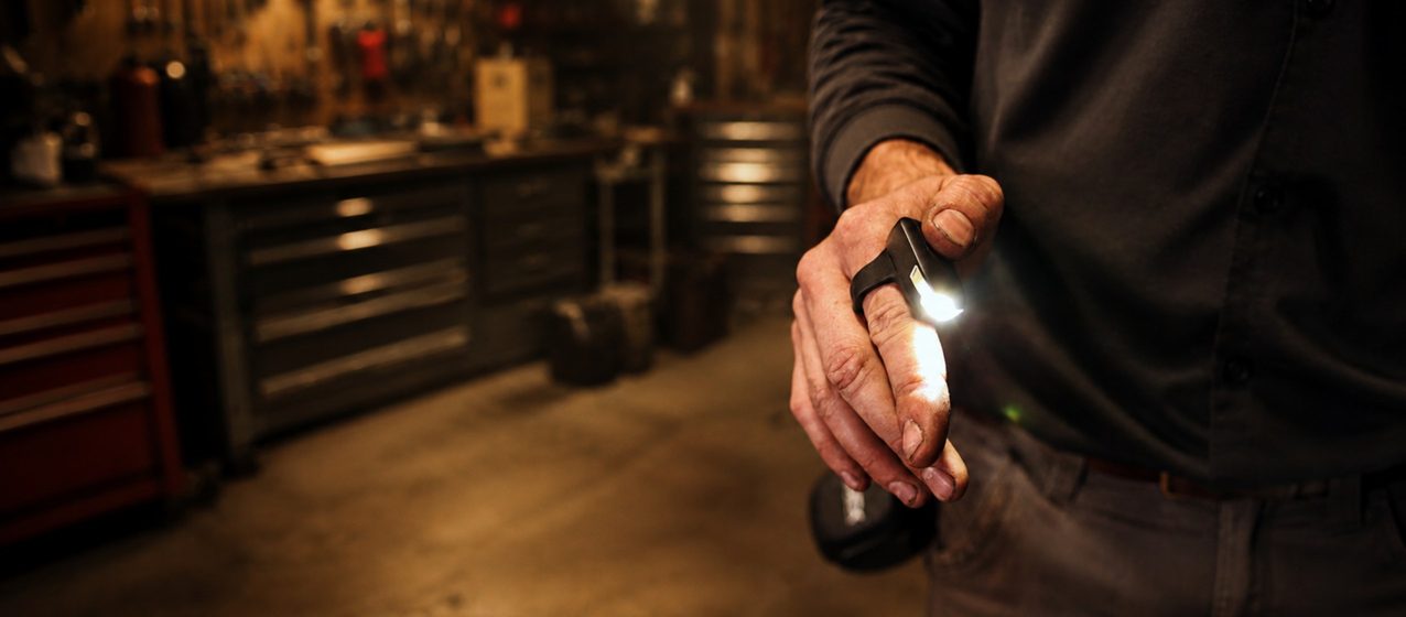 A person in a workshop holding a small flashlight that lights up their hand.