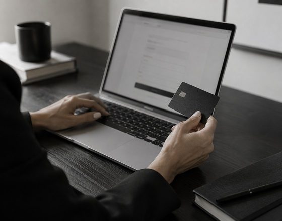 A person holding a bank card next to a laptop showing a checkout page on a dark desk.