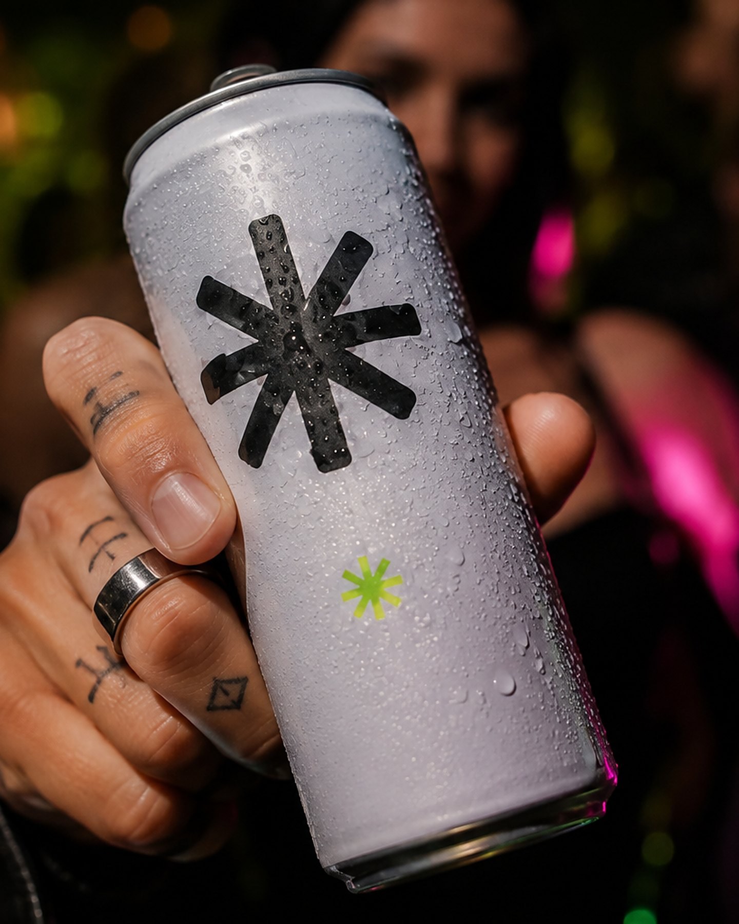 Hand holding a chilled white beverage can marked with an anonymizing asterisk at a nighttime event