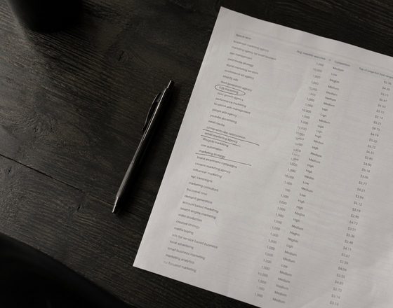 A printed list of search terms on white paper on a dark desk next to a pen.