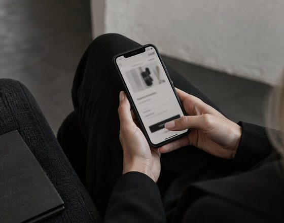 A person seated in an armchair holding a phone that shows a social media feed.