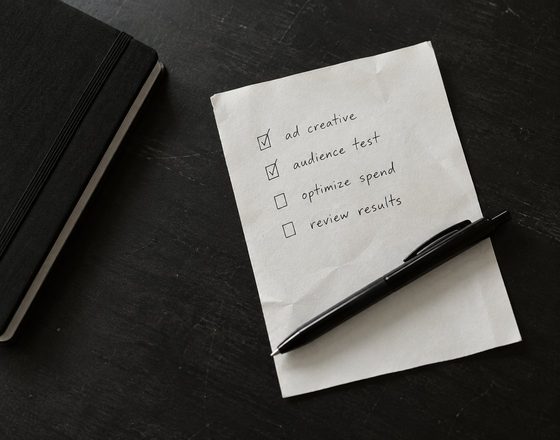 A handwritten checklist on white paper with a pen resting on it, on a dark desk.